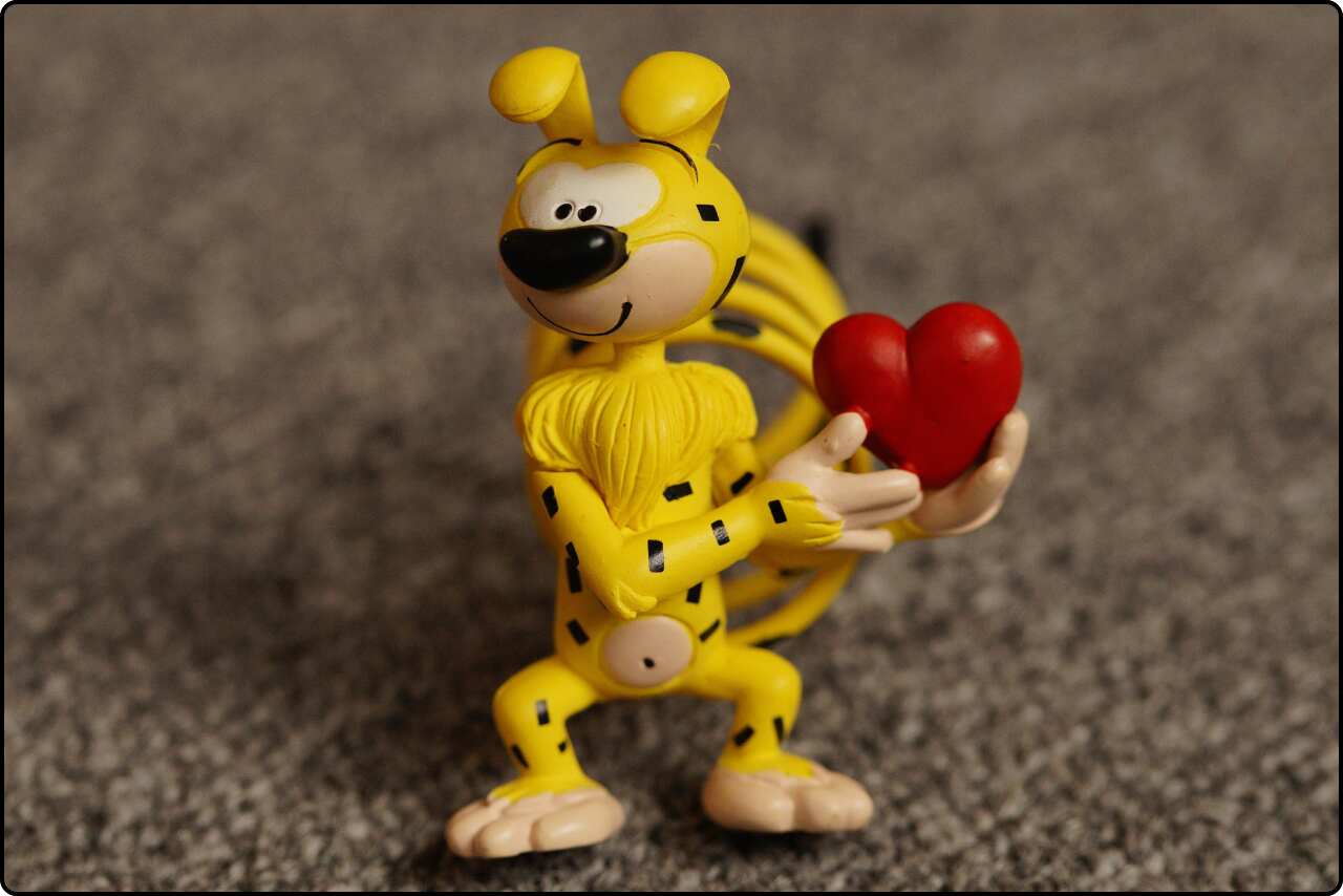 Yellow cartoon character holding a red heart with a smile.